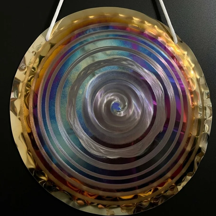 Handheld gong in violet and blue heat tones with concentric rings around a hammered spiral